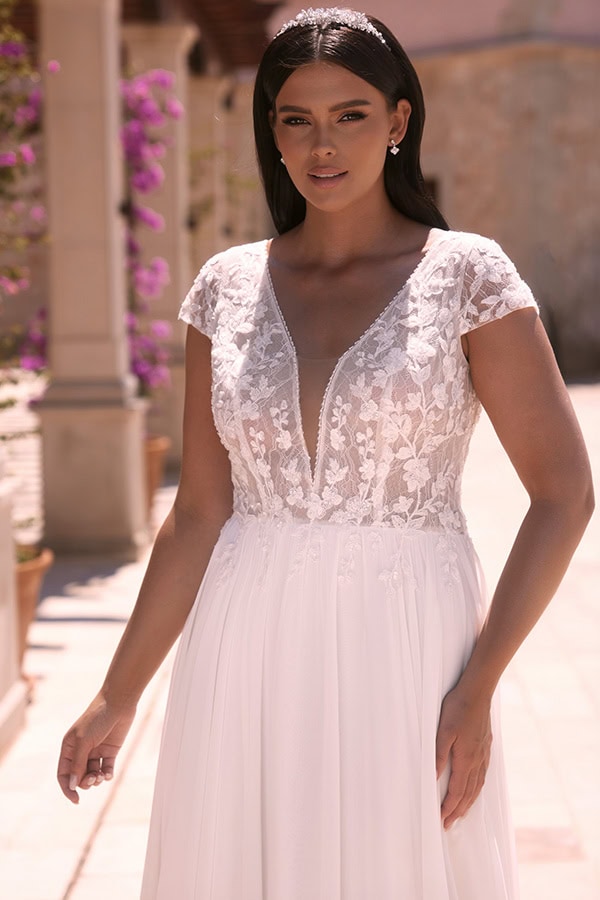 Eine dunkelhaarige Frau in einem eleganten weißen Brautkleid mit Spitzenoberteil