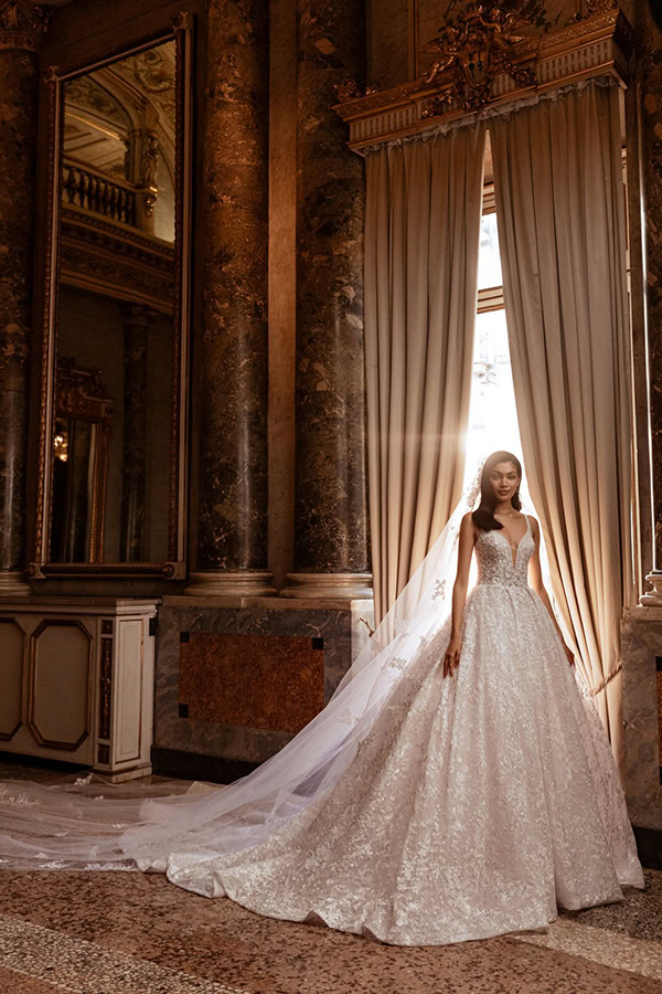 Eine Braut im weißen Spitzenkleid lächelt sanft in einem prunkvollen Saal