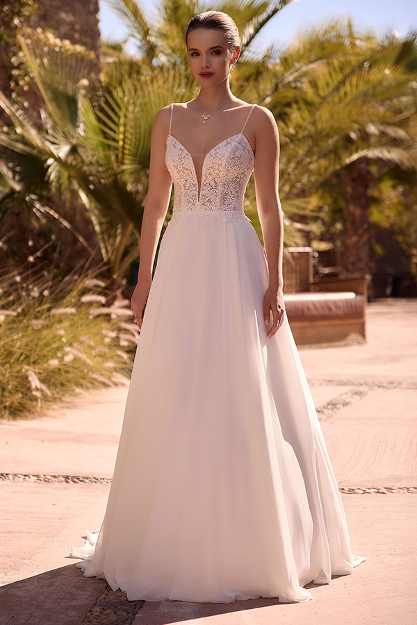 Eine junge Frau mit elegantem weißem Kleid und ernstem Gesichtsausdruck steht draußen