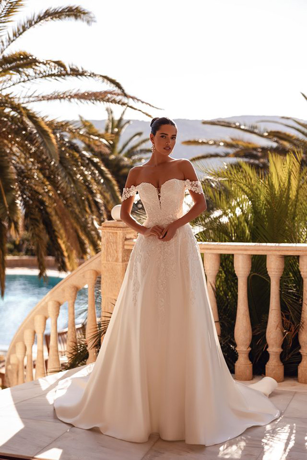 Eine elegant gekleidete Frau im cremefarbenen Brautkleid steht entspannt draußen