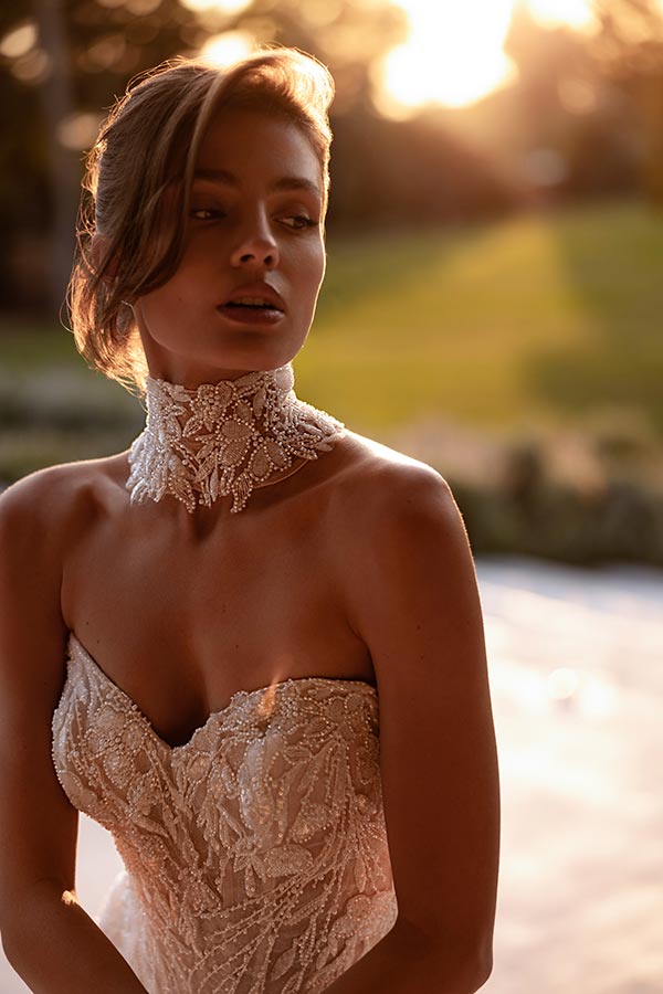 Junge Frau im eleganten cremefarbenen Kleid mit Perlenmuster blickt verträumt