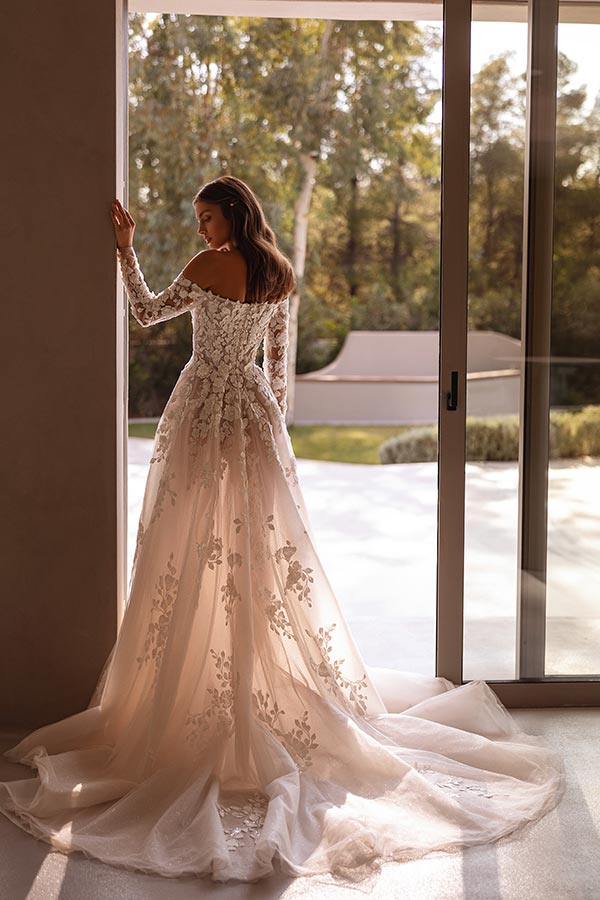 Eine Frau mit langen braunen Haaren trägt ein elegantes Spitzenkleid und blickt ruhig nach draußen