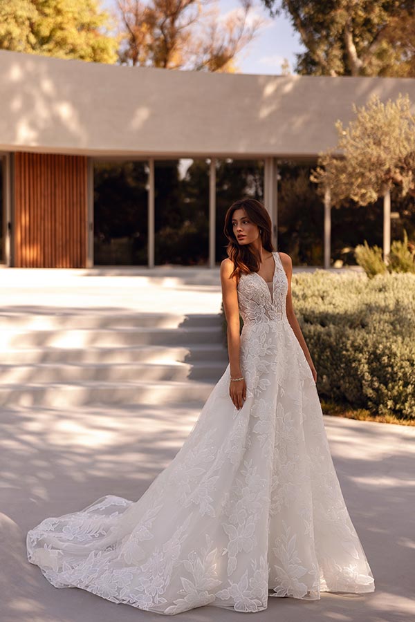 Braunhaarige Frau in elegantem weissem Brautkleid mit Spitzenmuster steht draußen