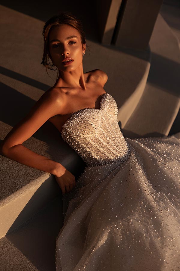 Junge Frau mit eleganter Pose und nachdenklichem Blick im glitzernden weißen Kleid