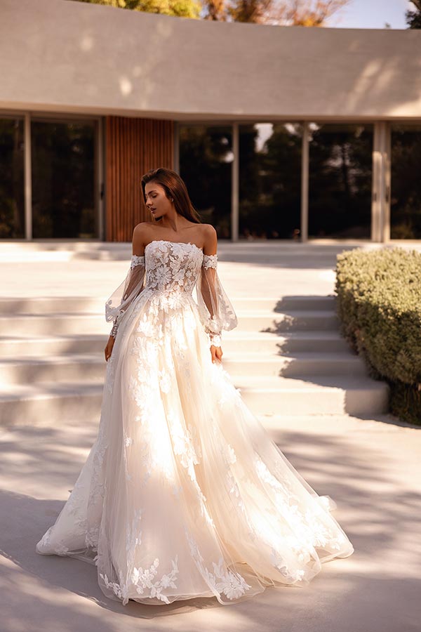 Junge Frau mit entspanntem Blick trägt ein cremefarbenes Brautkleid mit Blumenmuster