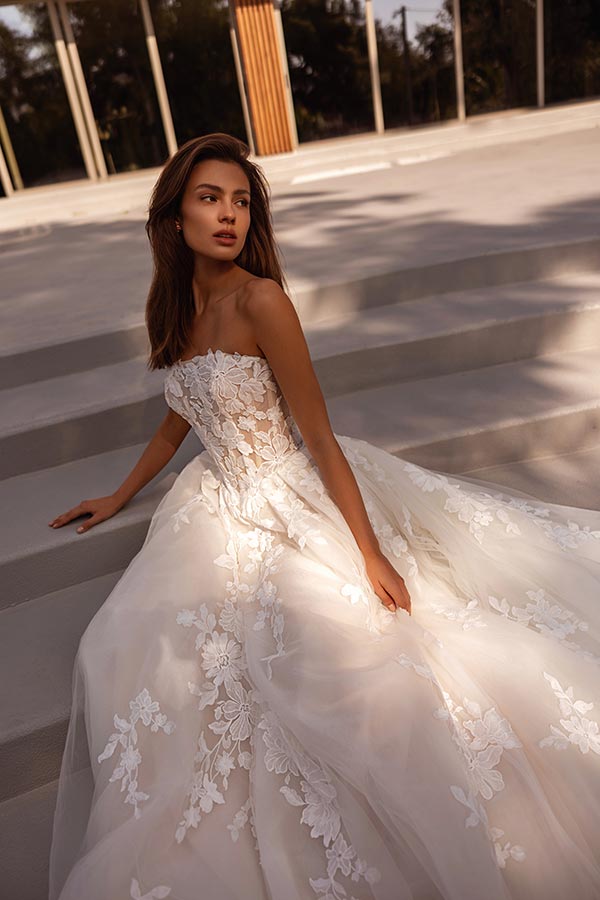 Junge Frau mit ernster Miene im weißen Spitzenkleid auf Treppe draußen sitzend