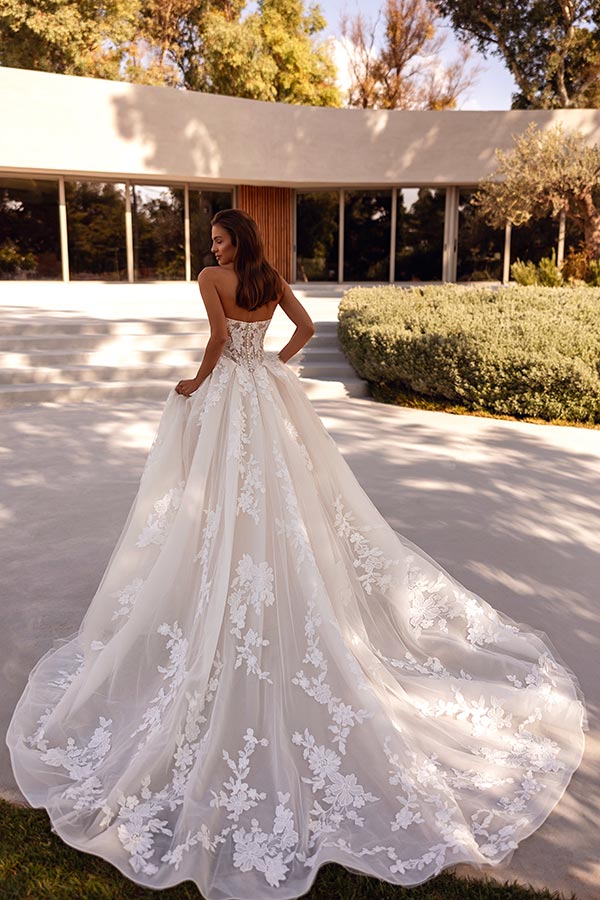 Eine lächelnde Frau in einem weißen Spitzenkleid steht im sonnigen Garten