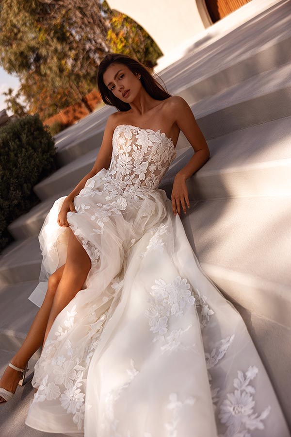 Eine junge Frau mit ernstem Blick trägt ein cremeweißes Kleid mit Spitzenmuster auf Treppen