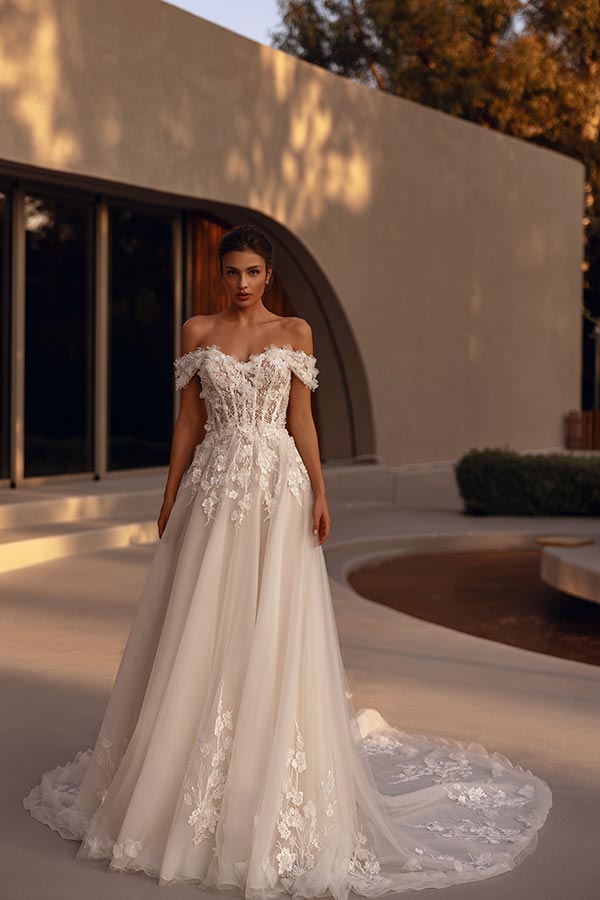 Eine junge Frau mit ernstem Blick trägt ein elegantes cremeweißes Brautkleid mit Spitze