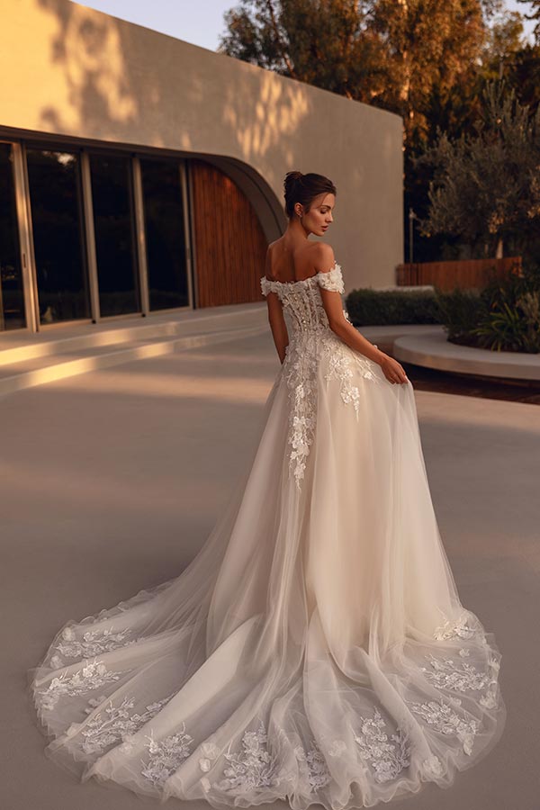 Braunhaarige Frau mit elegantem Lächeln trägt cremeweißes Brautkleid mit Spitzenrücken