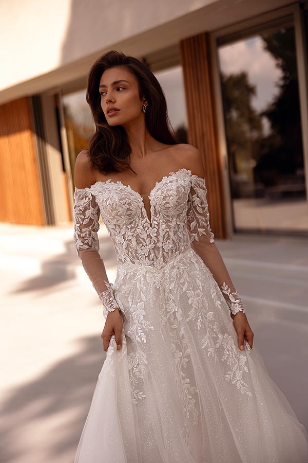 Eine Frau mit elegantem Ausdruck trägt ein weißes Spitzenkleid mit floralen Details