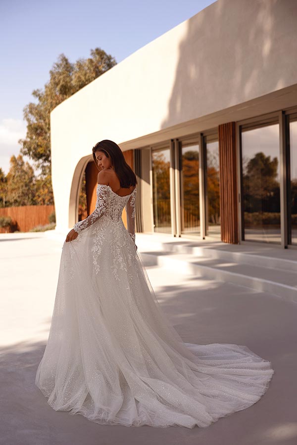 Eine Frau mit langen dunklen Haaren trägt ein elegantes weißes Brautkleid und blickt verträumt über die Schulter