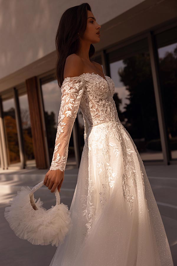 Junge Frau im eleganten weißen Brautkleid mit Spitzenärmeln hält weiße Tasche