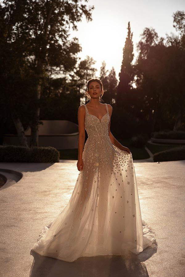 Eine junge Frau mit ernstem Blick trägt ein glitzerndes cremefarbenes Abendkleid bei Sonnenuntergang