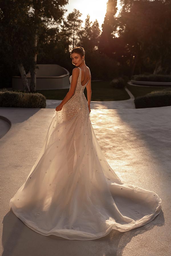 Eine junge Frau im funkelnden weißen Hochzeitskleid blickt lächelnd zurück