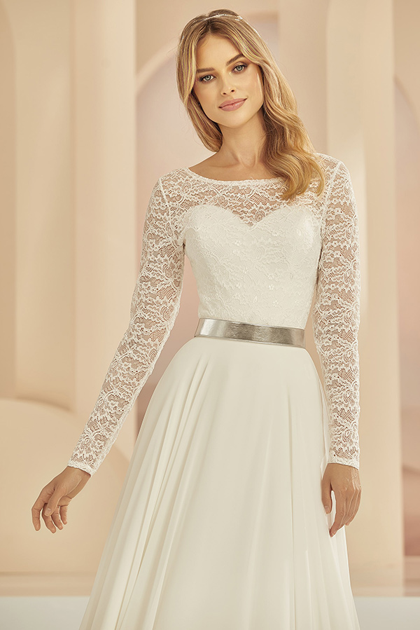 Junge Frau mit blondem Haar lächelt sanft in eleganter cremeweißer Spitzenrobe