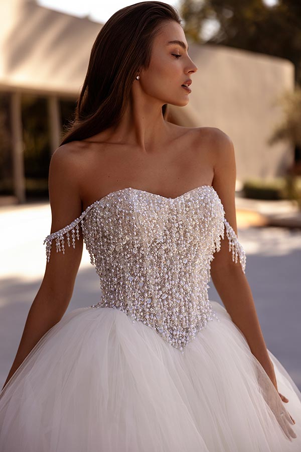 Frau mit langen braunen Haaren trägt ein weißes, verziertes, schulterfreies Kleid