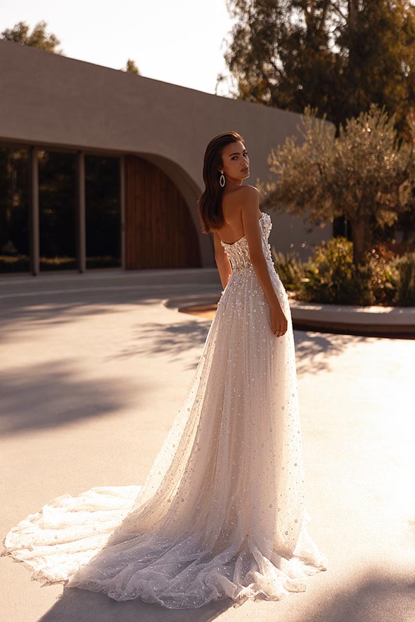 Junge Frau mit langen braunen Haaren schaut lächelnd über die Schulter im glitzernden weißen Kleid