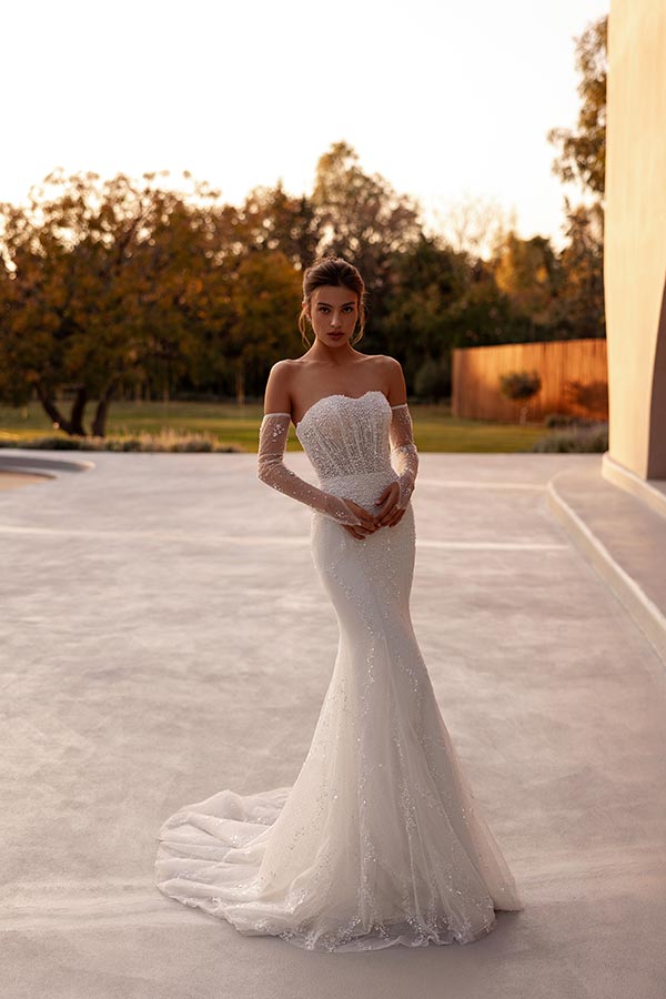 Eine junge Frau mit elegantem Gesichtsausdruck trägt ein weißes Brautkleid im Garten