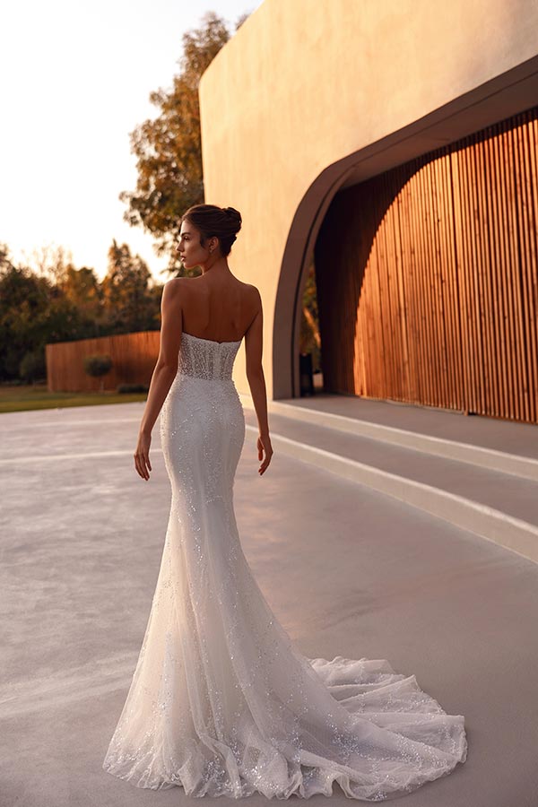 Eine Frau im eleganten weißen Brautkleid steht mit ruhigem Blick im Abendlicht