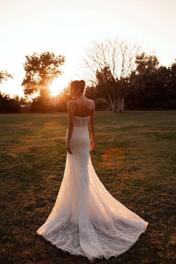 Eine Frau im weißen Brautkleid steht elegant auf einer Wiese bei Sonnenuntergang