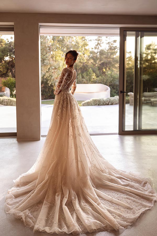 Eine Frau mit elegantem Ausdruck trägt ein langes, cremefarbenes Brautkleid mit Spitze