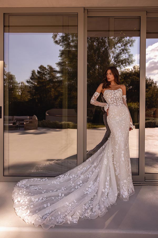 Eine Frau mit langen braunen Haaren trägt ein elegantes weißes Spitzenkleid und blickt ruhig