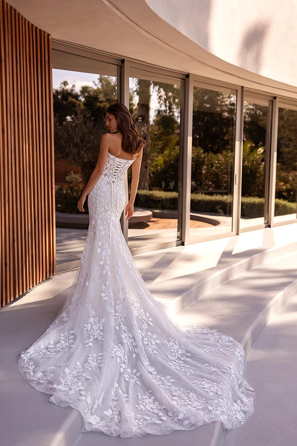 Eine Frau mit langen braunen Haaren trägt ein elegantes weißes Spitzenkleid mit langer Schleppe