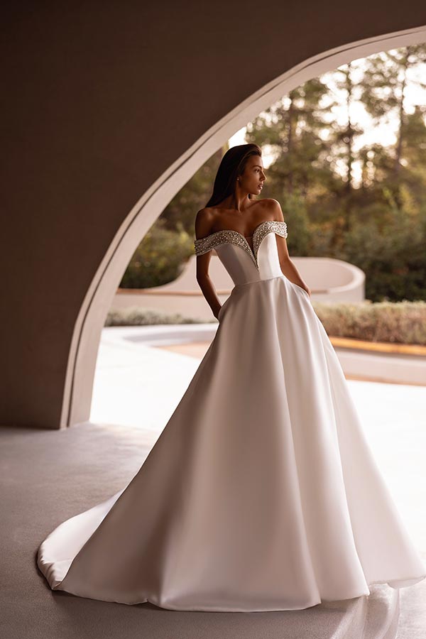 Eine Frau mit ernstem Blick trägt ein elegantes cremeweißes Ballkleid mit Perlenbesatz