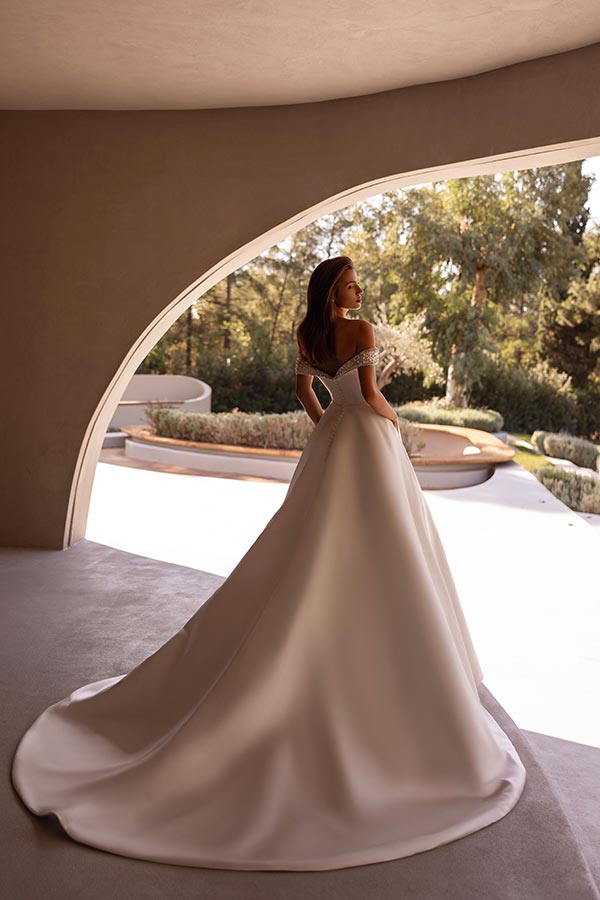 Eine lächelnde Frau in einem weißen Brautkleid steht vor einem modernen Bogenfenster