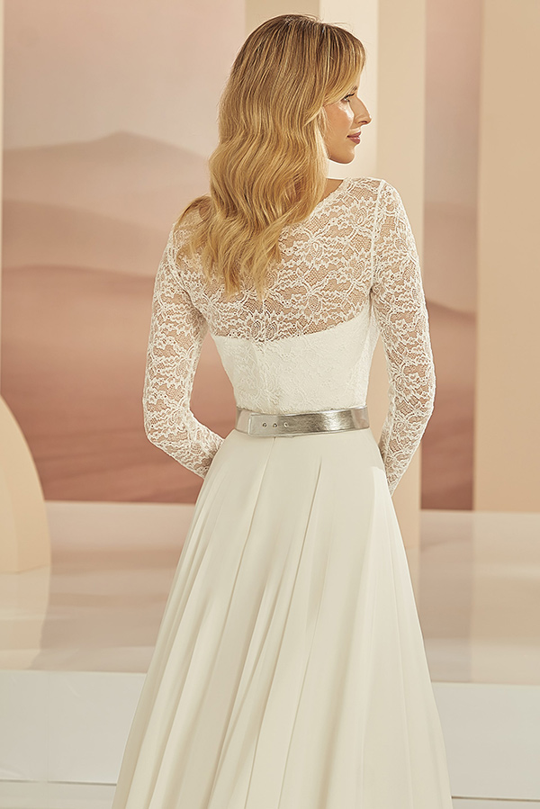 Eine Frau mit welligem blondem Haar trägt ein elegantes Spitzenkleid in Cremeweiß