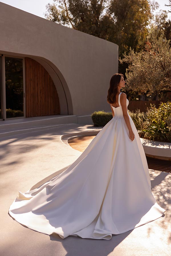 Eine Frau mit braunen Haaren trägt ein elegantes weißes Brautkleid im Garten