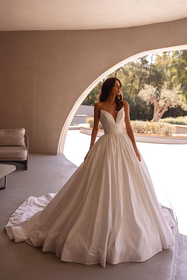 Eine Frau im eleganten weißen Brautkleid blickt verträumt aus dem Fenster