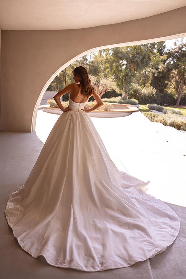 Eine Frau in einem eleganten weißen Brautkleid steht mit dem Rücken zur Kamera