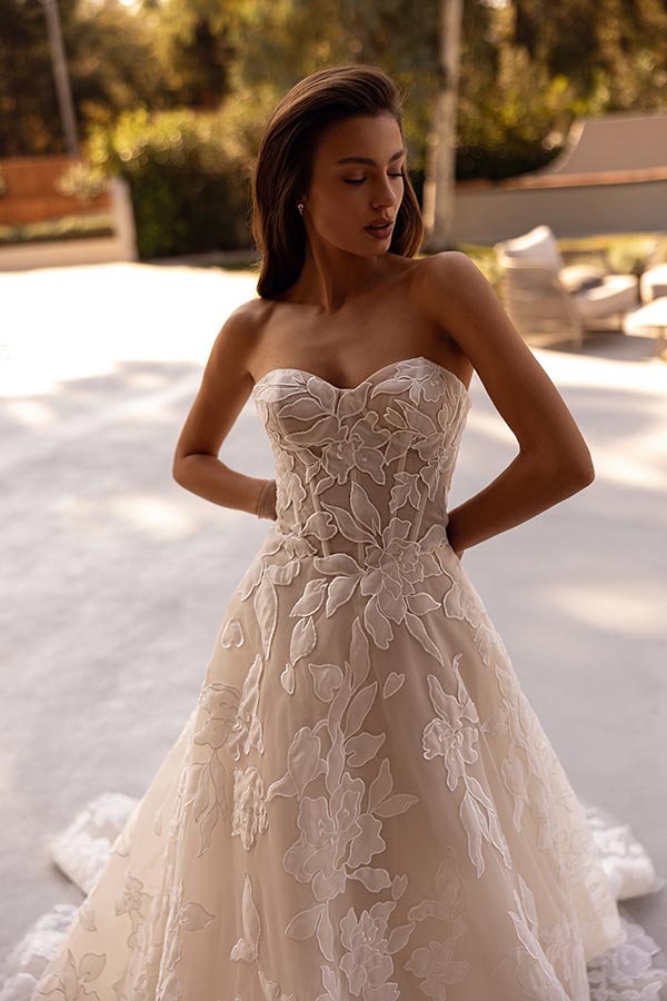 Eine junge Frau im cremefarbenen Brautkleid mit floralen Mustern schaut ruhig nach unten