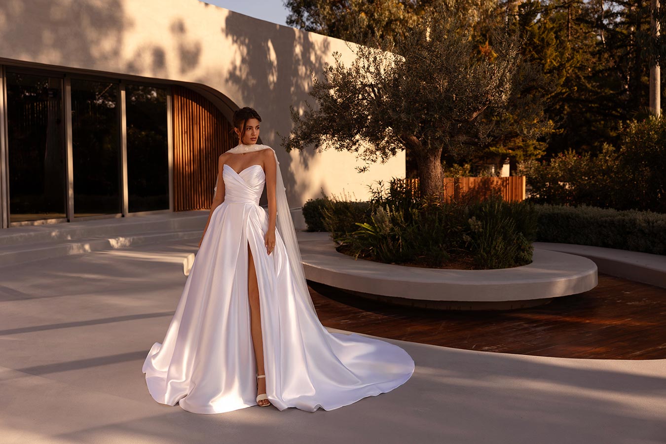 Eine junge Frau mit neutralem Gesichtsausdruck trägt ein elegantes weißes Kleid draußen