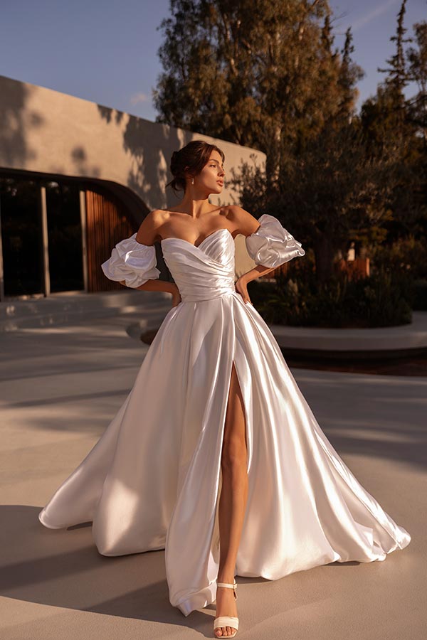 Elegante Frau in weißem Kleid mit Beinschlitz und voluminösen Ärmeln wirkt stolz