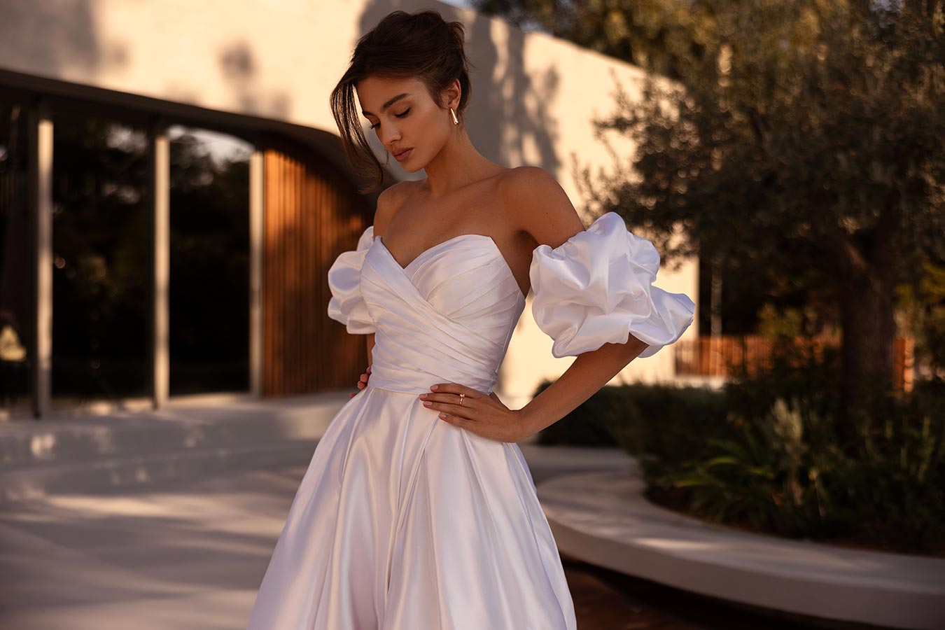 Eine junge Frau mit ernstem Blick in weißem Kleid mit voluminösen Ärmeln draußen