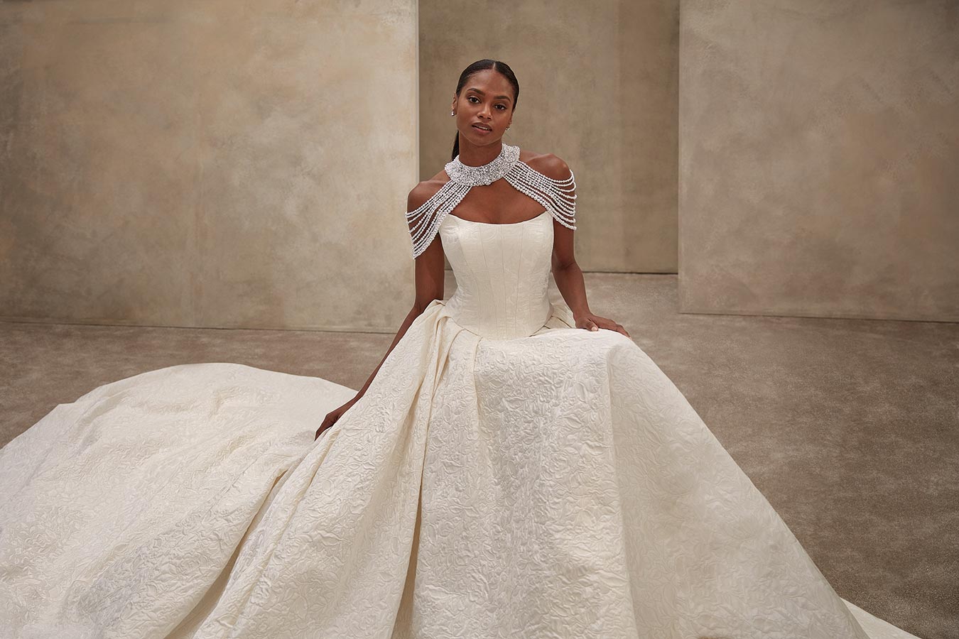 Eine elegant gekleidete Frau im elfenbeinfarbenen Brautkleid mit aufwendigem Schmuck und ruhigem Gesichtsausdruck