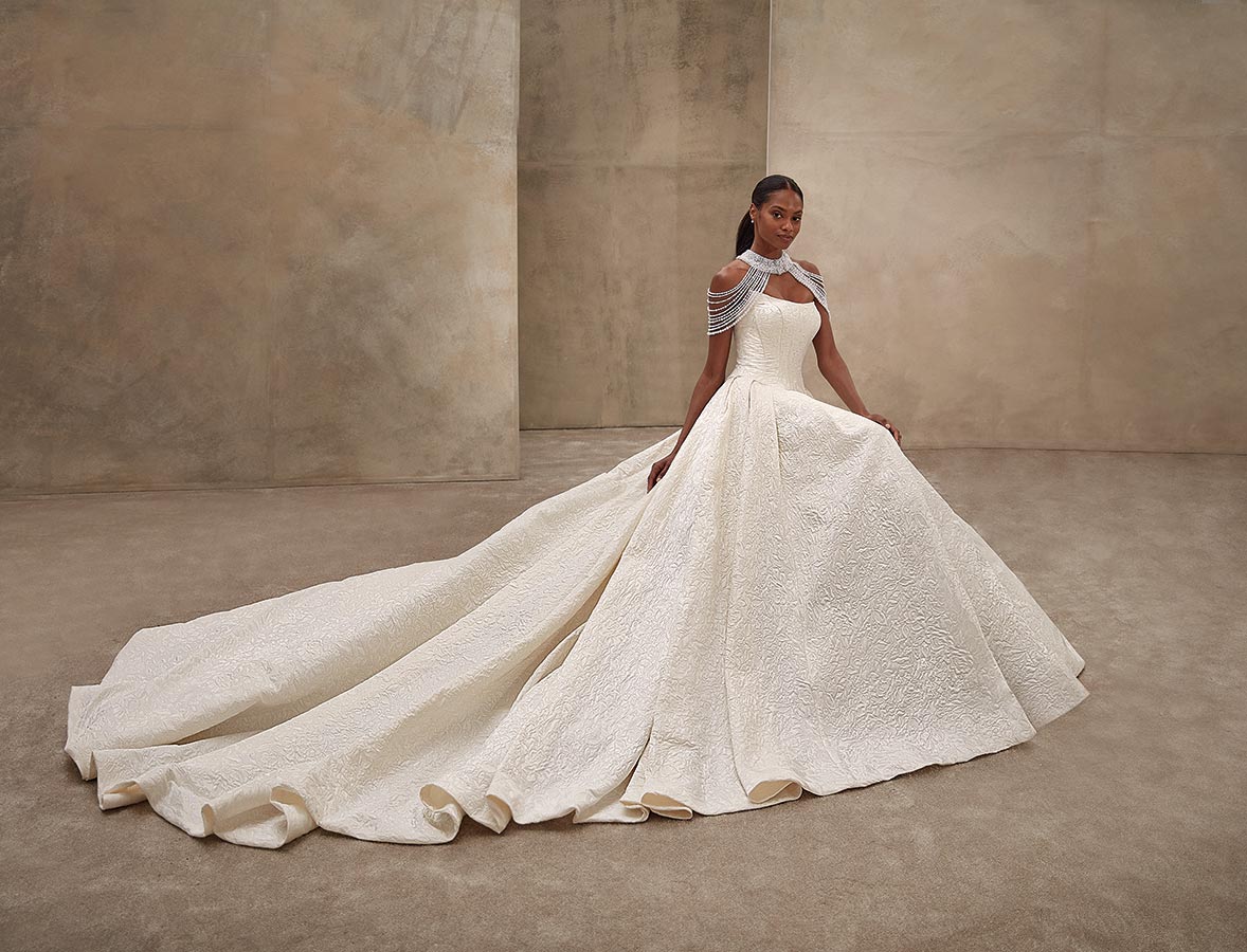 Eine elegante Frau mit ernstem Blick trägt ein auffälliges elfenbeinfarbenes Kleid mit langer Schleppe