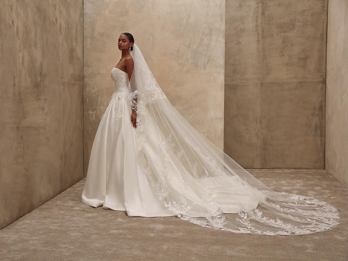 Eine Frau im weißen Brautkleid mit langer Schleppe und neutralem Gesichtsausdruck