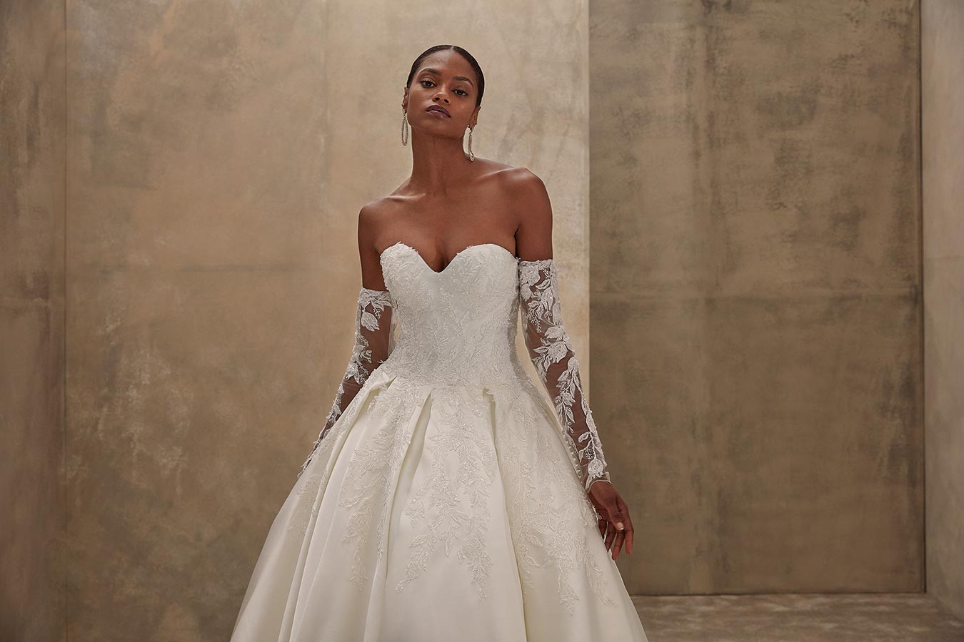 Eine elegante Frau im cremefarbenen Spitzen-Brautkleid schaut ernst in die Kamera