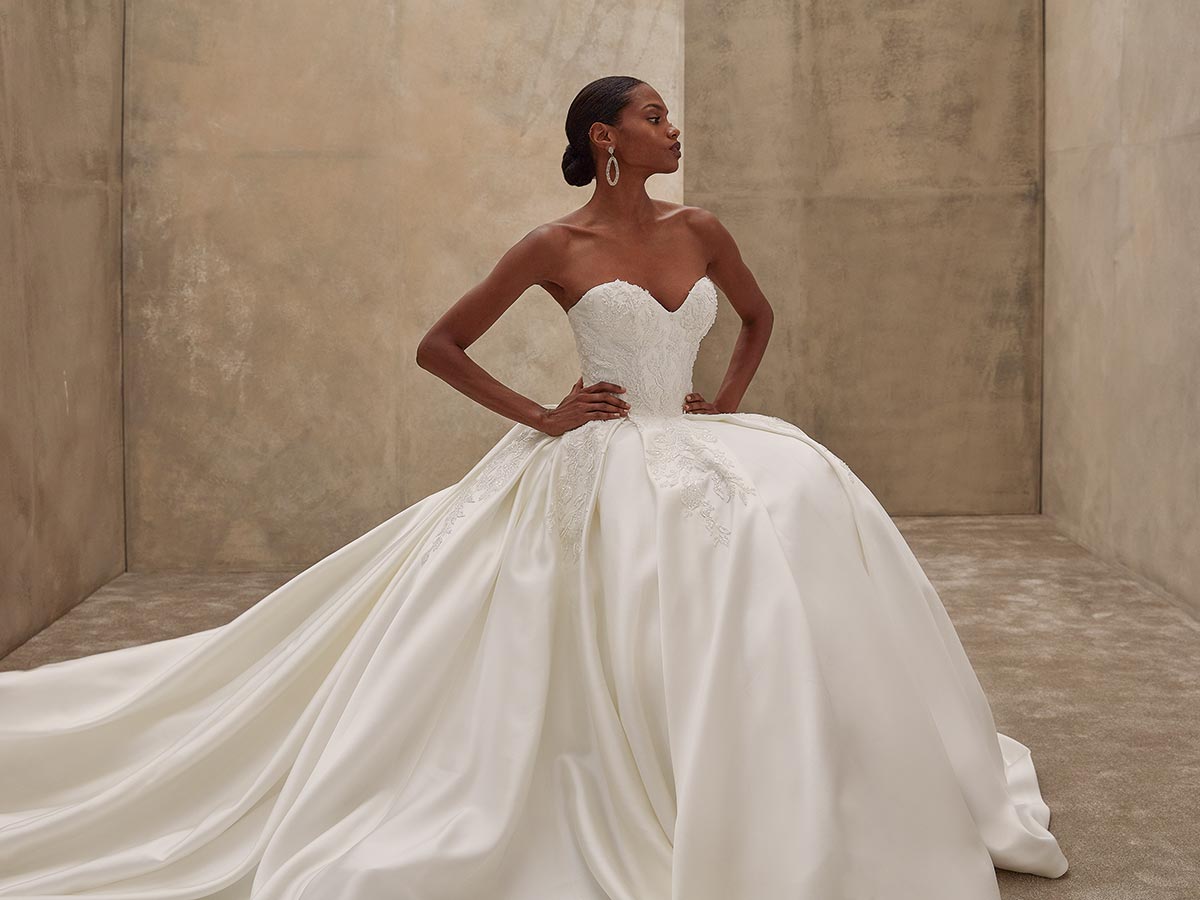 Eine Frau in einem eleganten weißen Brautkleid posiert stolz mit ernster Miene