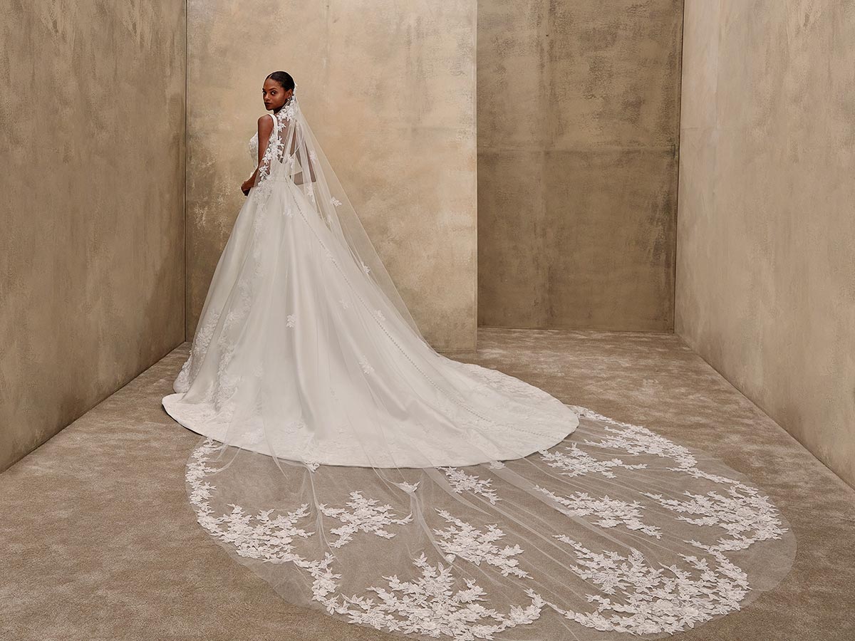 Eine Frau in elegantem weißen Brautkleid mit langer Spitzen-Schleppe blickt zurück