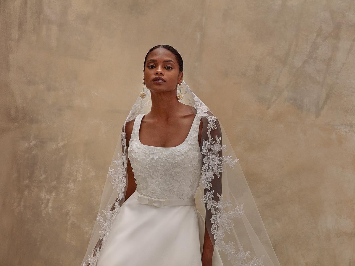 Eine Frau im weißen Brautkleid mit Spitzenstickerei blickt ruhig und würdevoll
