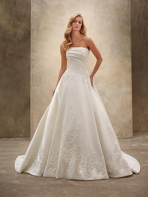 Eine blonde Frau trägt ein elegantes weißes Brautkleid mit feinen Spitzenmustern