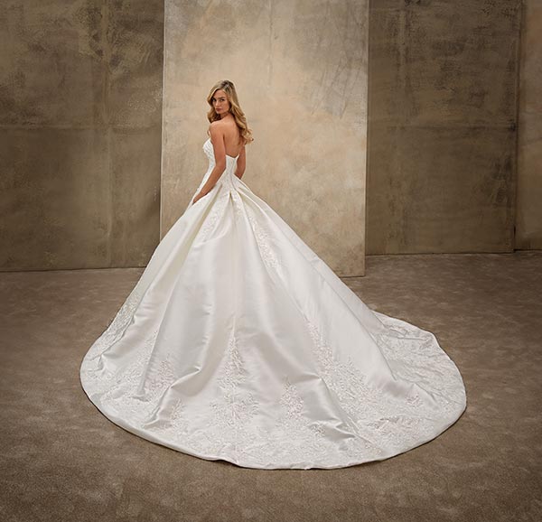 Junge Frau mit ernstem Blick trägt elegantes weißes Brautkleid mit langer Schleppe