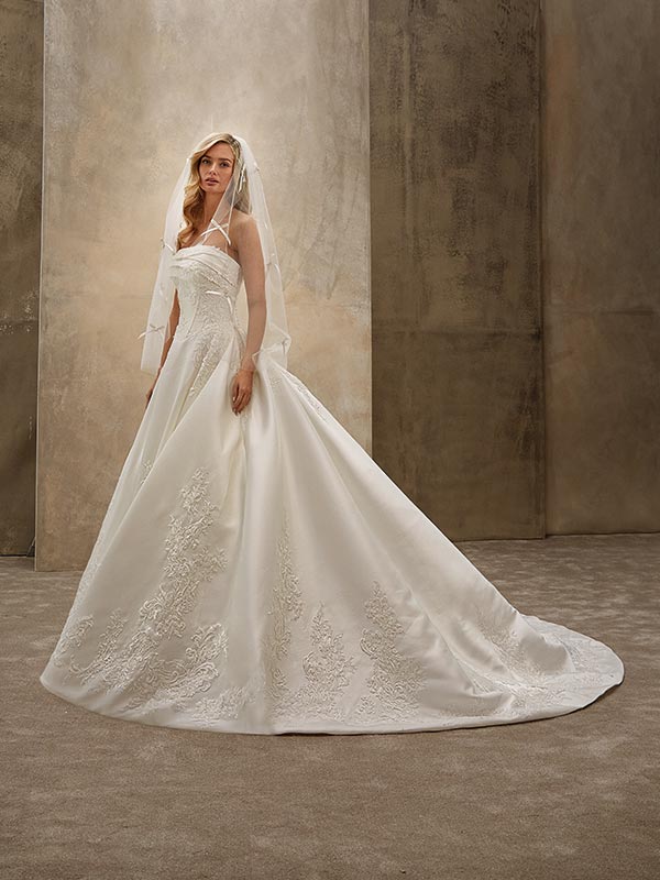 Junge Frau im weißen Brautkleid mit Schleier schaut ernst und steht vor beigefarbenem Hintergrund