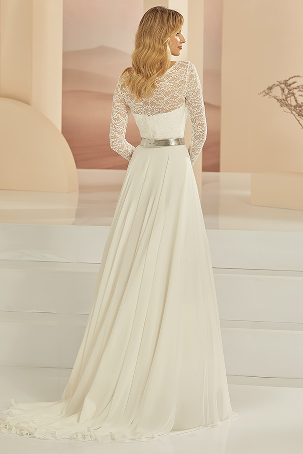 Eine Frau mit blonden Wellen trägt ein elegantes weißes Kleid mit Spitze und silbernem Gürtel