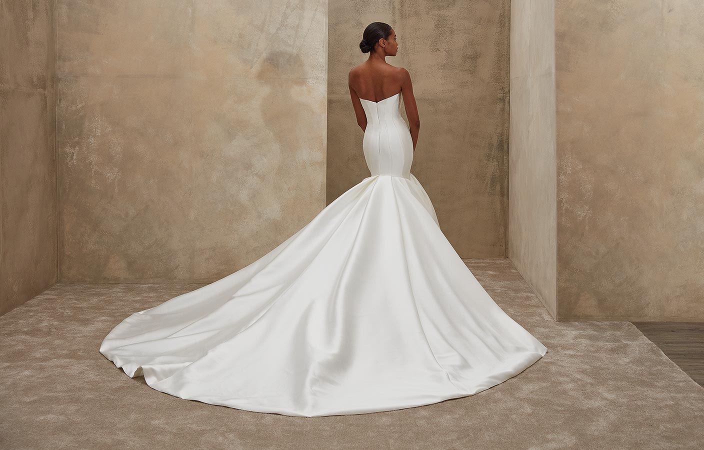 Eine Frau steht mit ernstem Blick in einem weißen, eleganten, schulterfreien Brautkleid